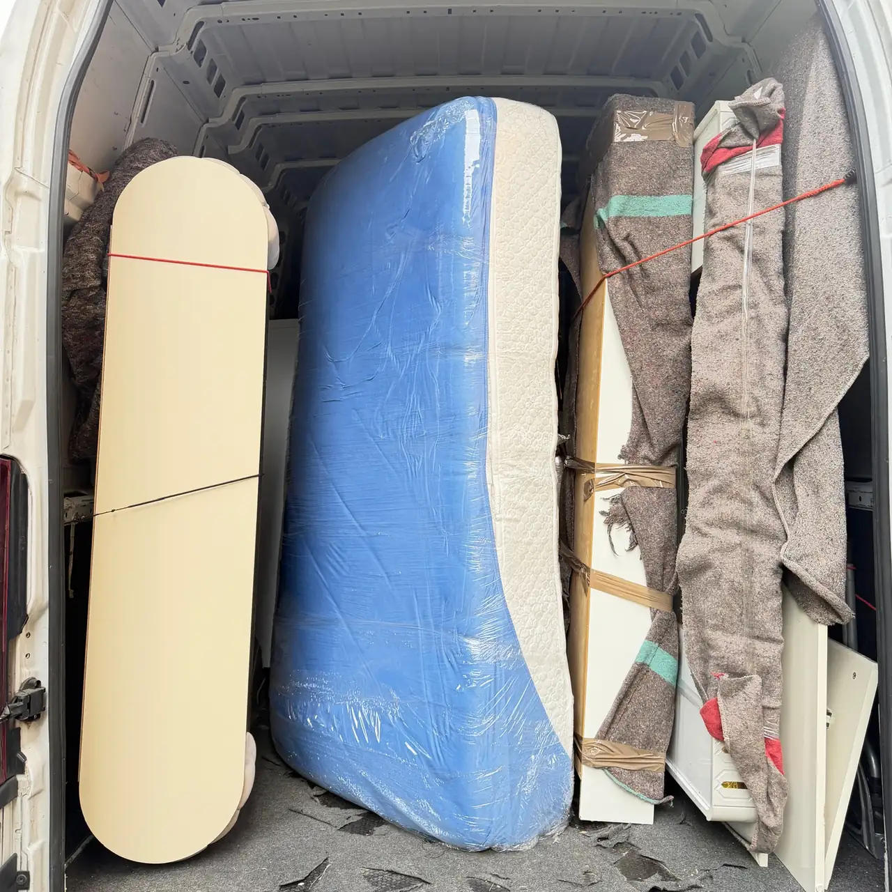 Mattress, headboard and furniture wrapped and protected with blankets and straps inside the Baipor van