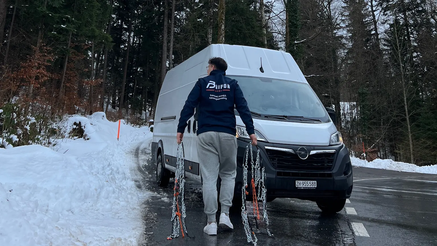 A Baipor team member, seen from behind, carrying snow chains to the van on a snowy road