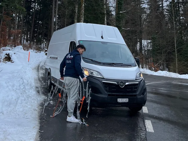 A Baipor worker fitting snow chains to the van on a snowy road in Switzerland