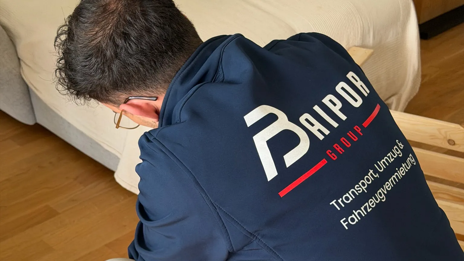 A Baipor fitter in a company hoodie, seen from behind, assembling a wooden bed at a customer’s home